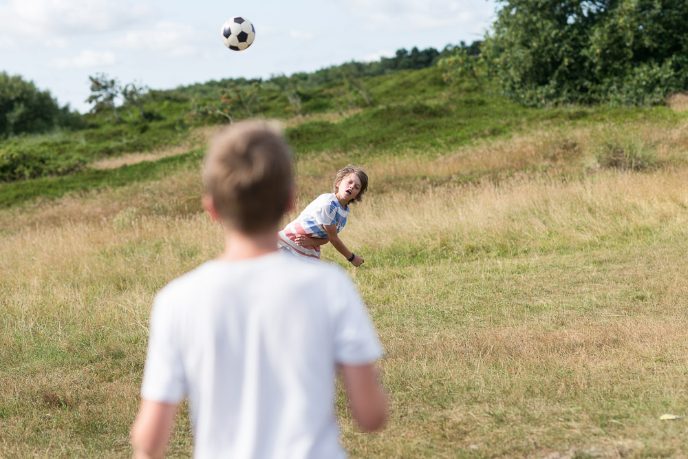 Zwei Jungen spielen Ball auf der Freifläche vorm Haus. Im Hintergrund Dünen.